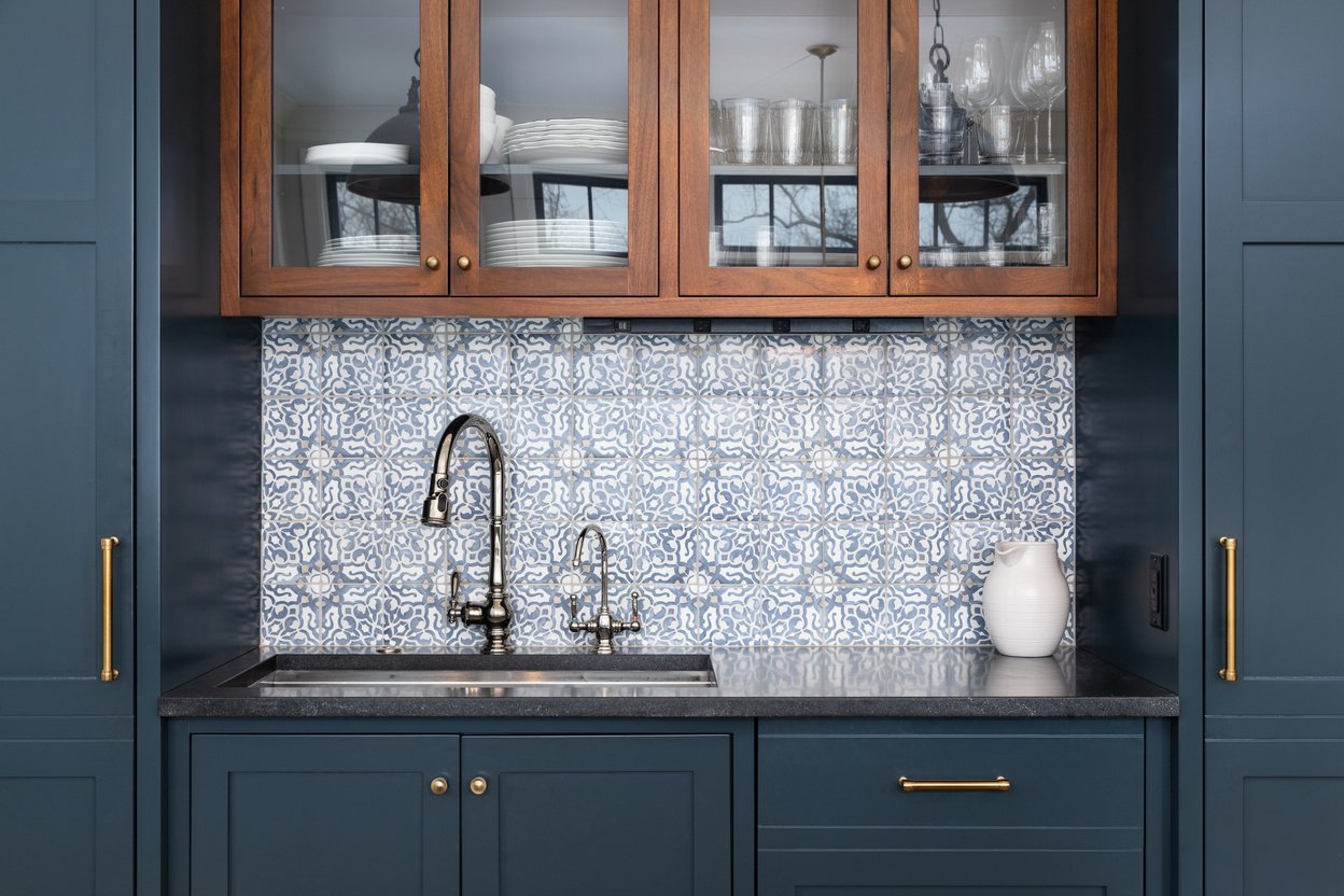 A kitchen sink detail with blue cabinets and tiled backsplash.