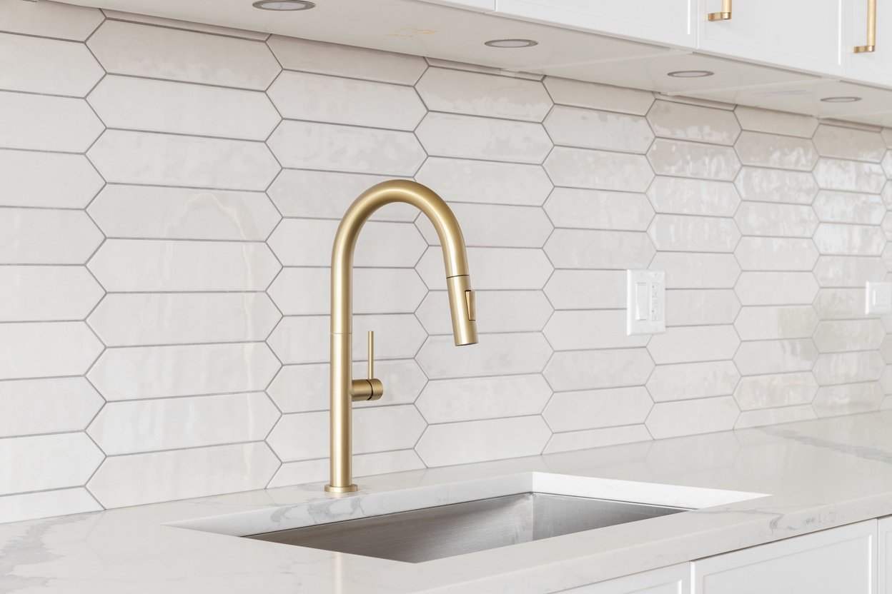 A kitchen detail with white cabinets, gold faucet, and tiled backsplash.